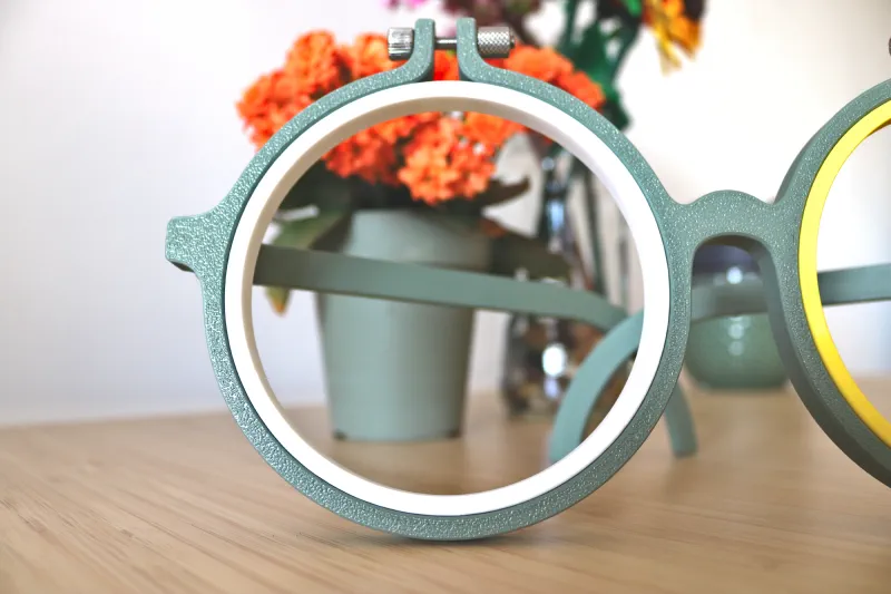 Left lens of the glasses 3D printed embroidery hoop framing orange flowers.